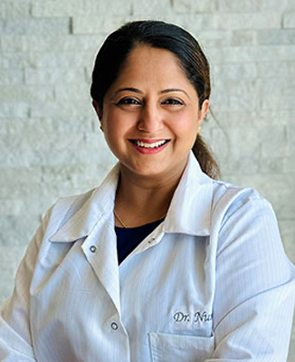 The image features a woman wearing a white coat, standing against a light-colored background. She is smiling and appears to be in a professional setting.