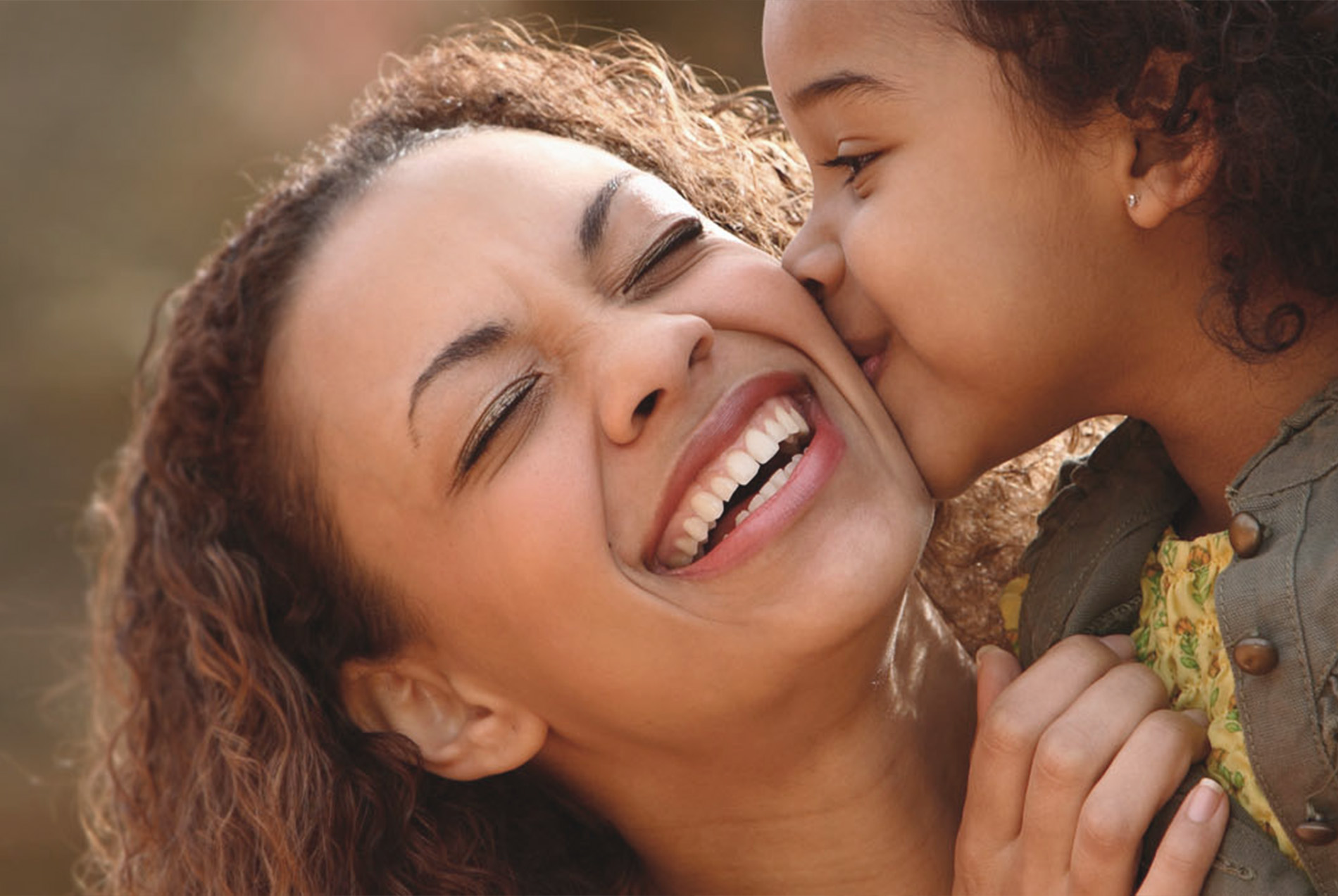 A woman with a child, both smiling and embracing, set against a blurred background.