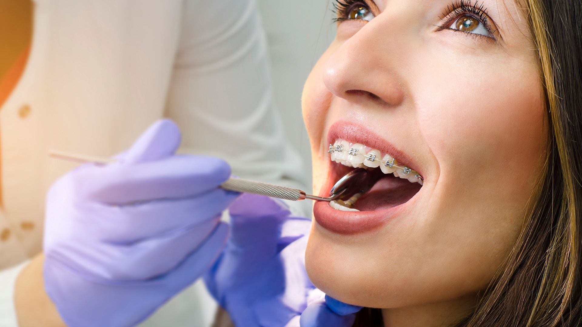 An image of a woman receiving dental care, with a dental hygienist performing a cleaning procedure using specialized tools.