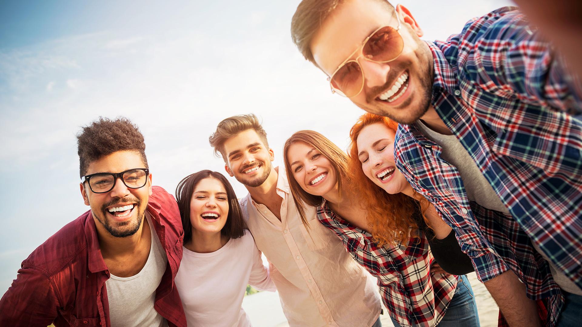 A group of smiling people, likely friends or family, posing for a selfie with their smartphones.