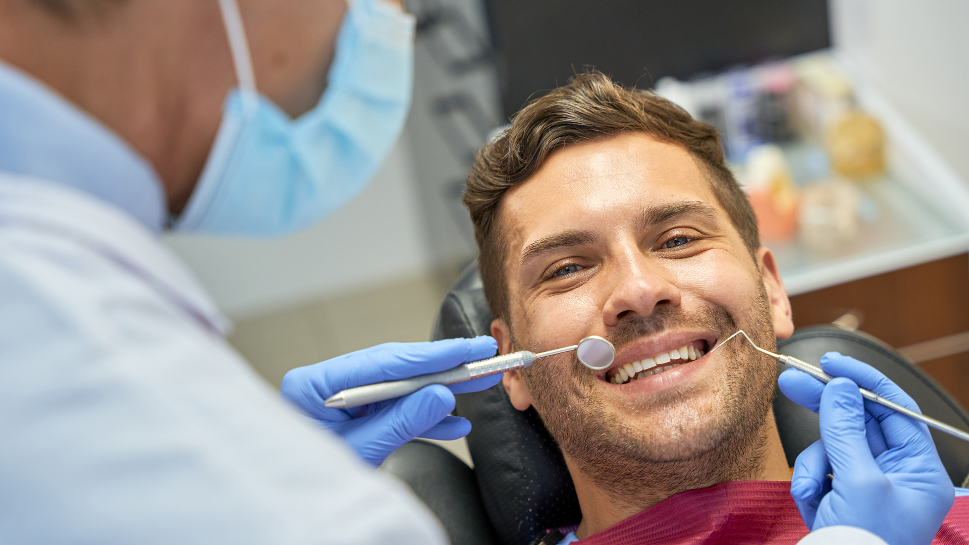 The image shows a person receiving dental care, with a dentist performing a procedure while the patient smiles and appears relaxed.