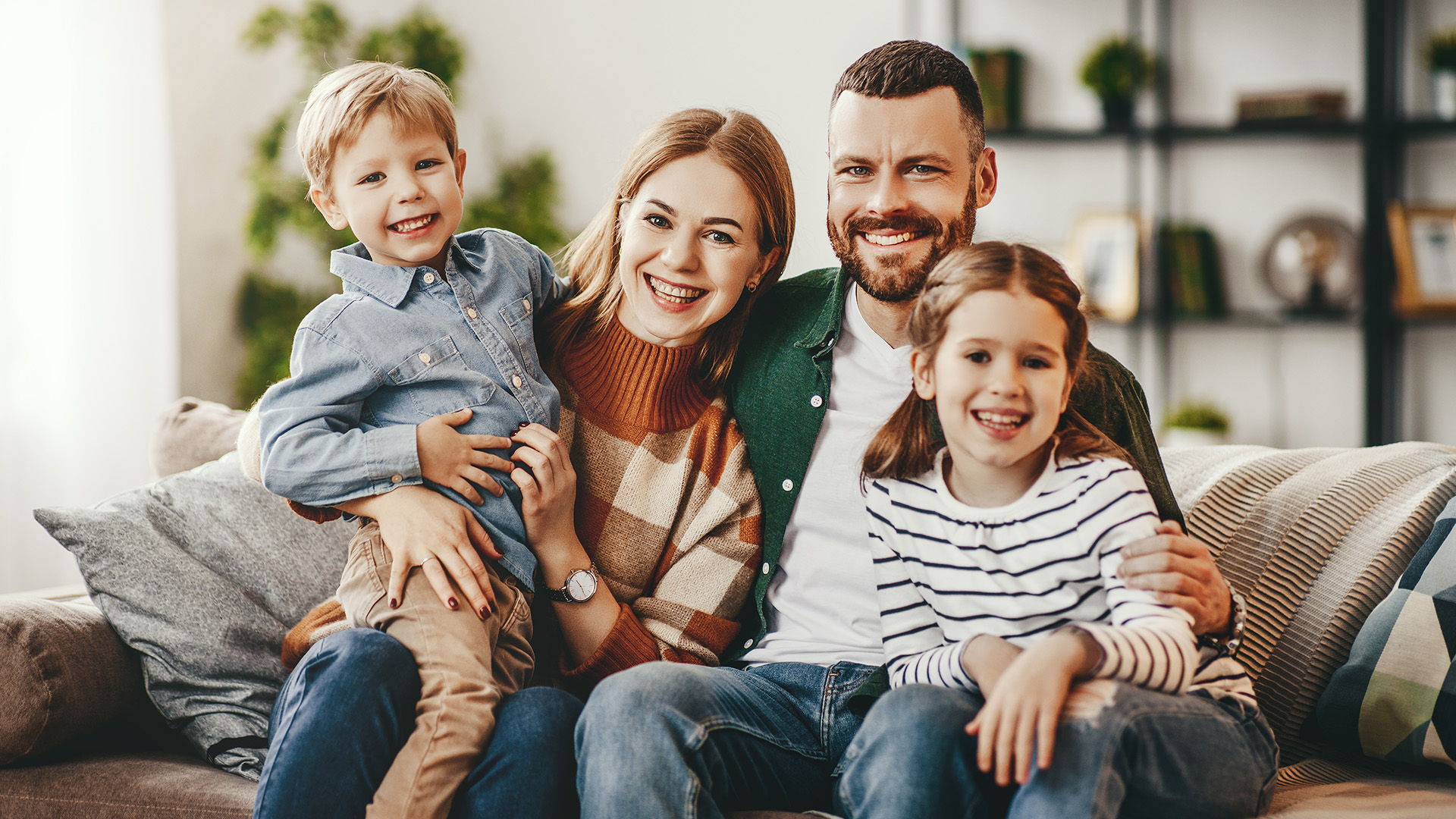The image depicts a family of four, a man, woman, and two children, posing together in a home setting.
