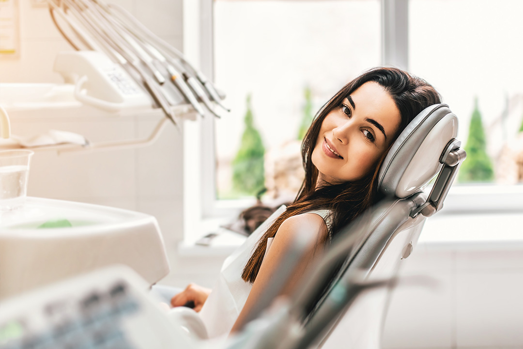 A woman sitting in a dental chair with a smile, looking directly at the camera.