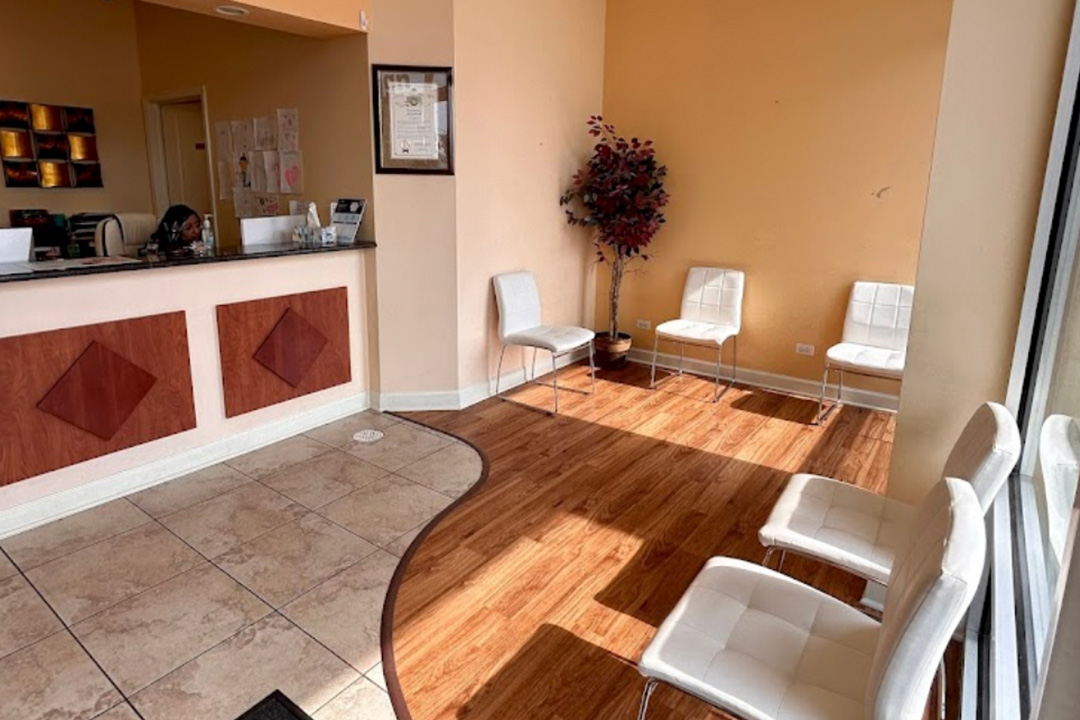 The image shows an interior view of a waiting area within a building, featuring a reception desk with a counter and chairs on the other side.