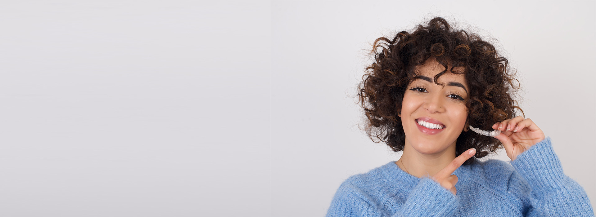 The image is a photograph of a person smiling and holding a smartphone to their ear, with a blurred background that suggests a studio setting.