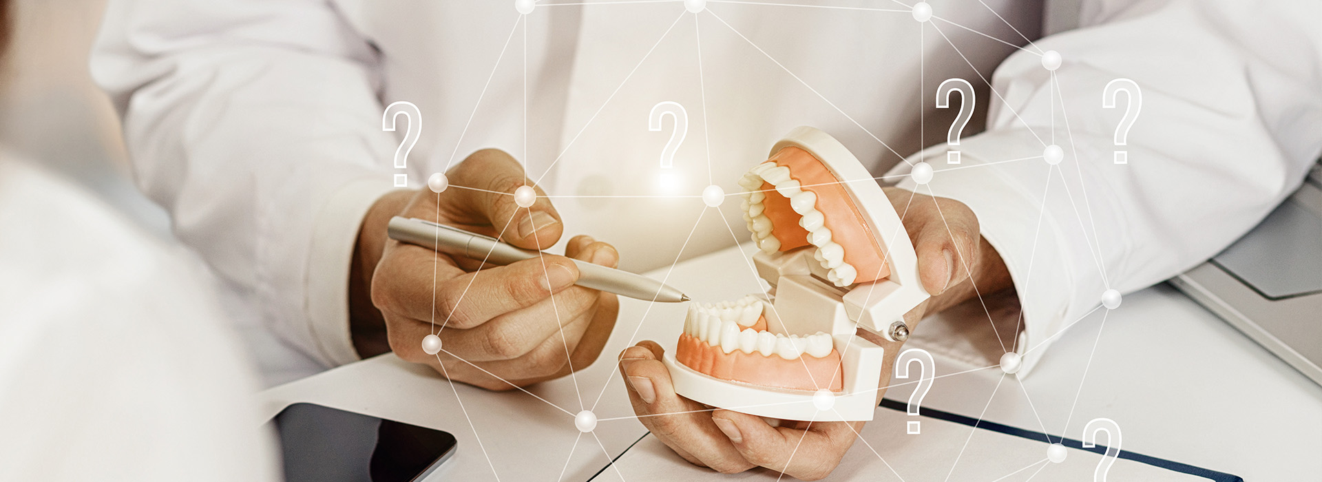 A person s hand holding a tooth model over an open laptop screen with dental implant information displayed.