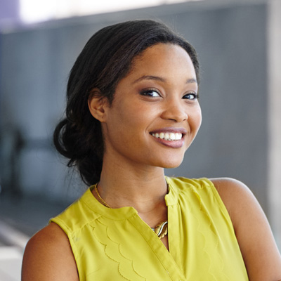 The image features a young woman with dark hair smiling at the camera. She is wearing a yellow top and has her hair styled up.