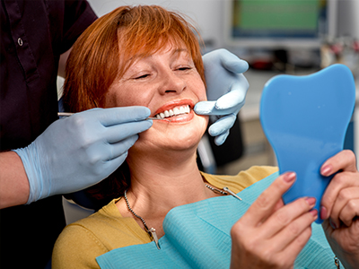 A woman receiving dental care, with a hygienist adjusting her teeth and holding up a blue model of a tooth.