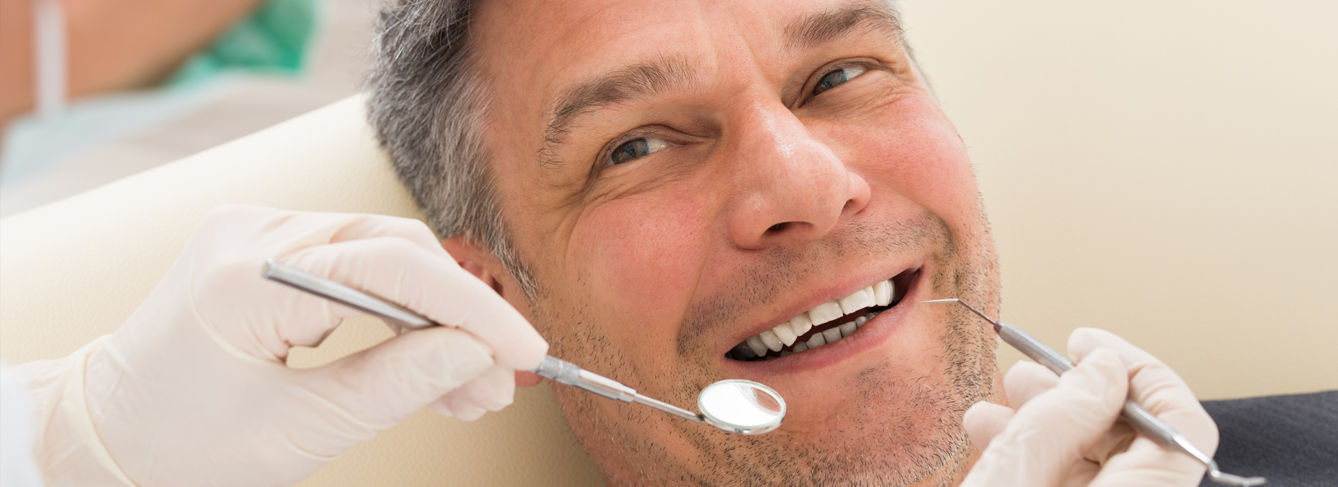 Man in a dental chair receiving dental treatment, with a smiling expression and a hygienist working on his teeth.