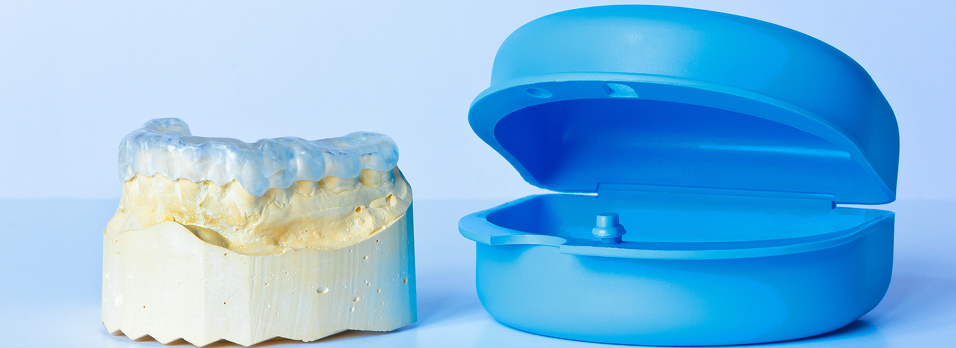 The image shows a transparent blue dental impression tray alongside a yellow resin model of a tooth, both against a white background.