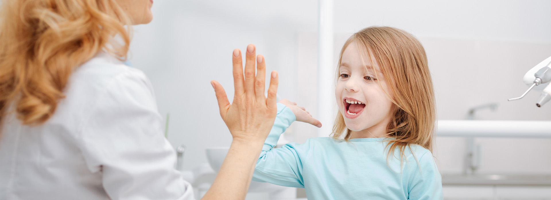 A photograph of a woman and a young girl in a dental setting, with the woman gesturing towards the child.