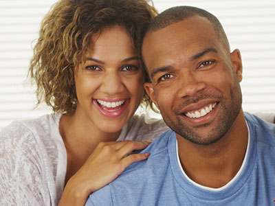 A man and a woman posing for a photo with smiles on their faces, the man has short hair and is wearing a blue t-shirt.
