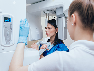 Woman in blue medical gown inspecting advanced imaging equipment with a technician.