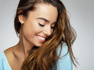 A woman with long brown hair, wearing a blue top, smiling and looking off to the side.