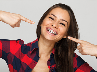 A woman with a wide smile and her finger on her nose, pointing towards the camera.