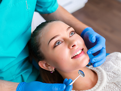 An image of a dental professional performing a procedure on a patient, with the patient seated and smiling while wearing blue gloves.