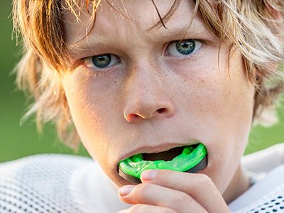 A young boy with blonde hair is holding a green toothbrush in his mouth.