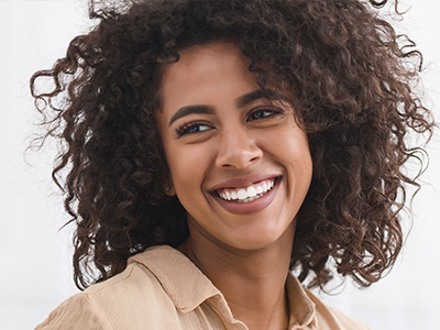 The image is a portrait of a smiling woman with curly hair, wearing a light-colored top.